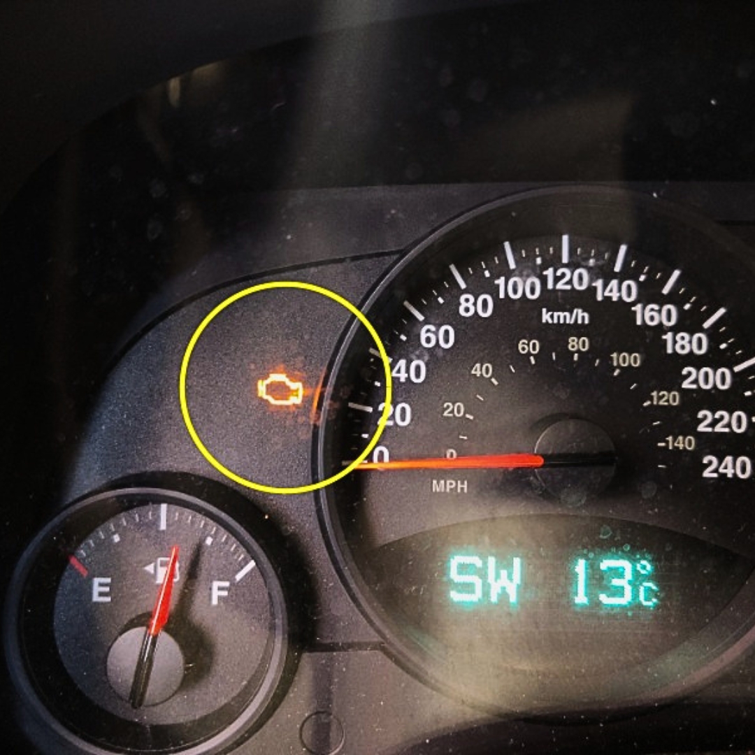 Car dashboard with the check engine light on near the speedometer fuel gauge to the left and a sw °c readout below
